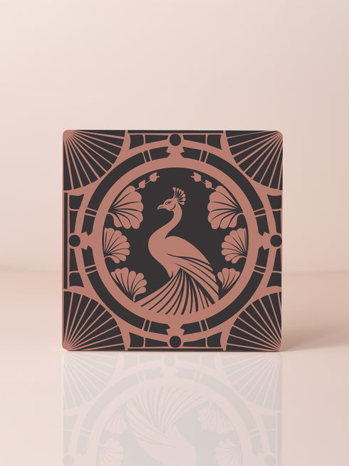 Square ceramic coaster featuring a detailed Art Deco peacock design in copper tones, surrounded by shell motifs and geometric fan patterns on a dark charcoal background, with protective cork base.